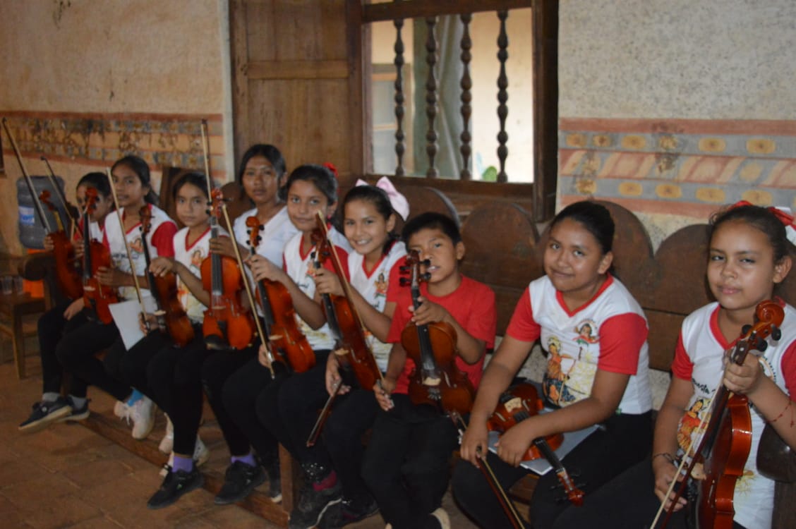 Niños músicos sentados en una banca dentro de una iglesia en Santa Ana de Velasco durante el festival de música barroca de 2025.